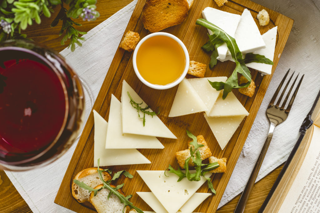 top view cheese plate a variety of cheeses with honey arugula and crackers on the board